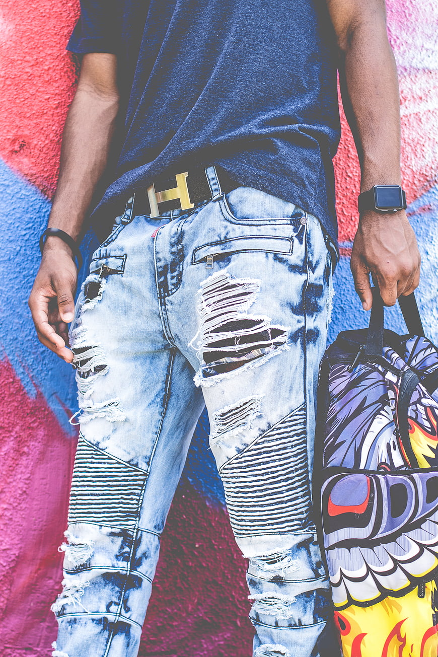 Man in ripped jeans and gold belt against graffiti wall