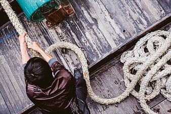 Overhead view of fisherman pulling thick rope on wooden boat deck