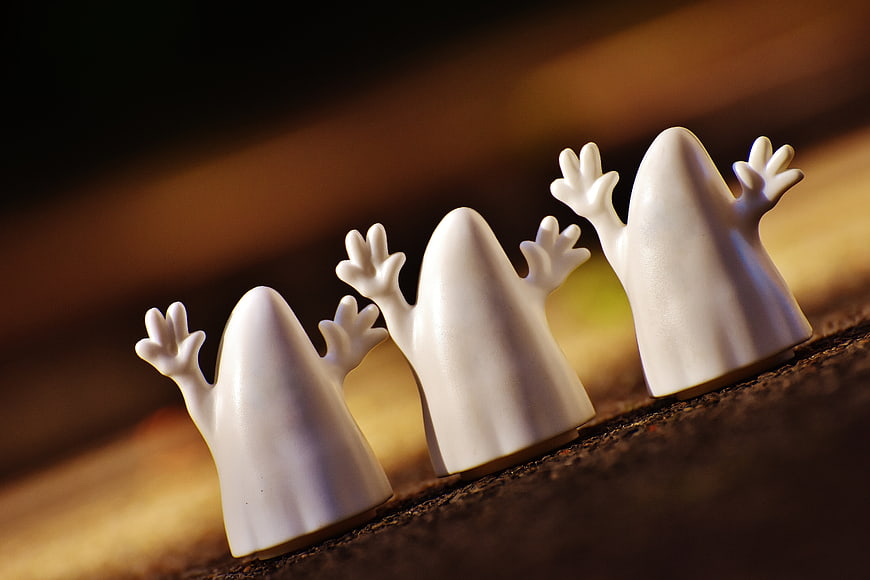 Cute white ghost figurines lined up on a wooden surface