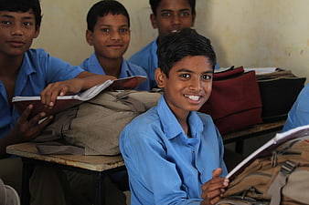 Smiling school boy in blue uniform holding book in classroom