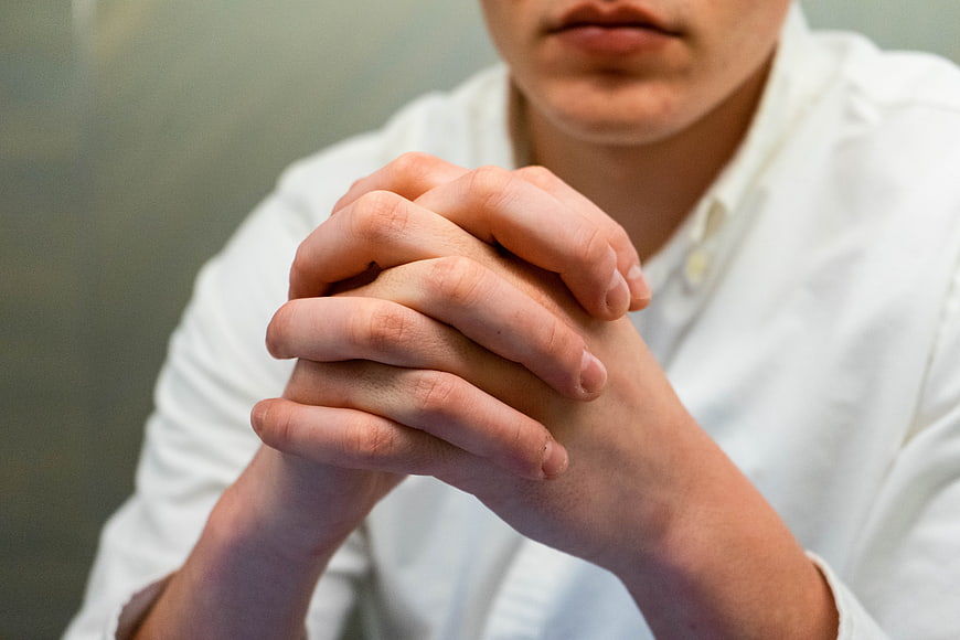 Close-up of man with clasped hands in white shirt