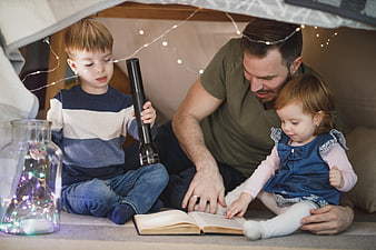 Father reading to children in cozy blanket fort with fairy lights