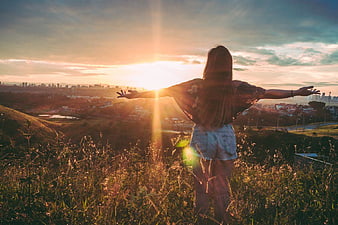 Woman with Arms Outstretched Watching Sunset Over City