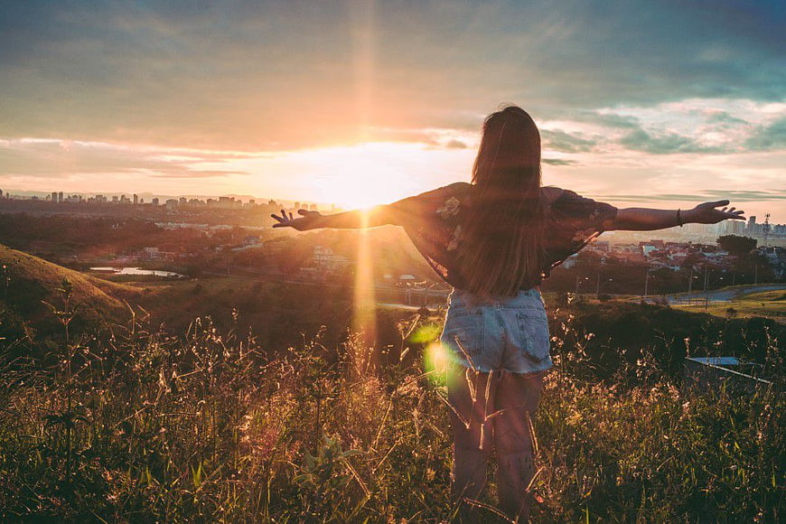 Woman with Arms Outstretched Watching Sunset Over City