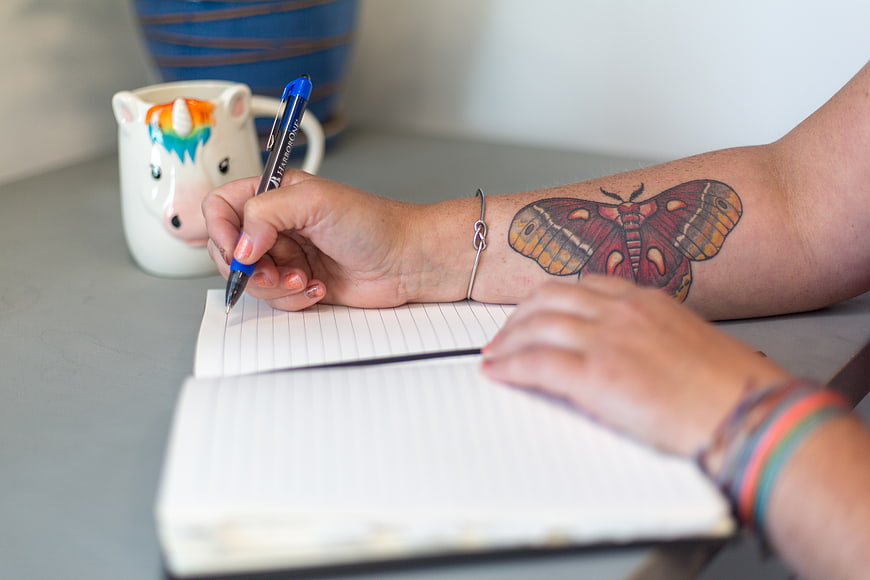 Woman writing in notebook with butterfly tattoo and unicorn mug