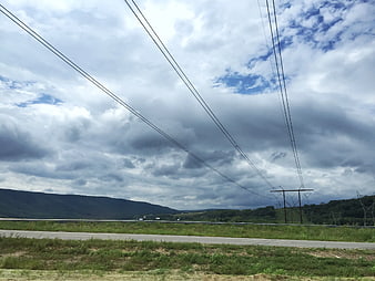 Power lines crossing a cloudy sky over a rural highway landscape