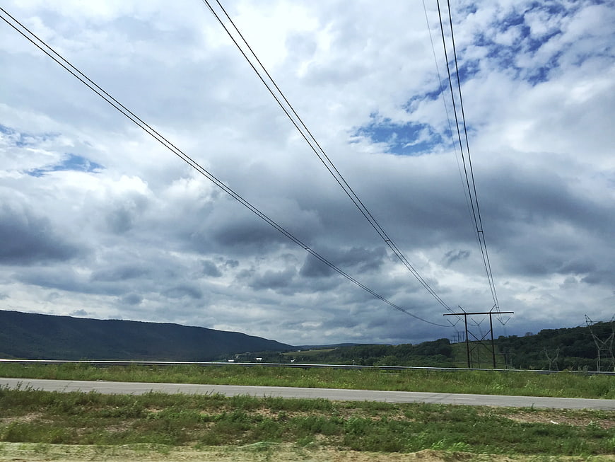Power lines crossing a cloudy sky over a rural highway landscape