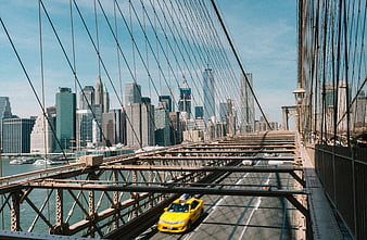 Yellow taxi driving on Brooklyn Bridge with Manhattan skyline