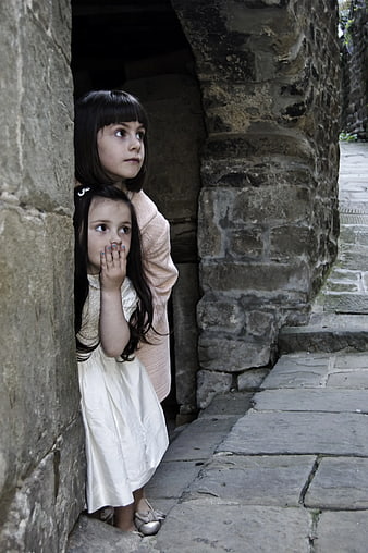Two young girls peeking from stone archway
