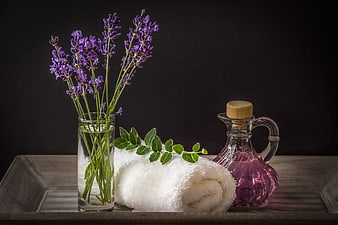 Lavender spa still life with rolled white towel and purple oil carafe
