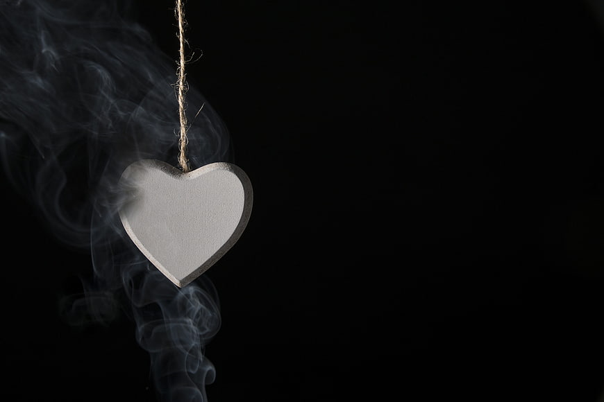 White wooden heart hanging with smoke on black background