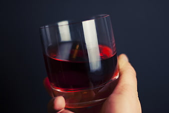 Hand holding glass of red liquid against dark background