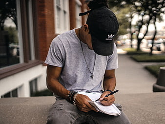 Man Writing in Notebook Outdoors Wearing Black Cap