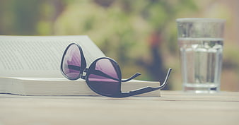 Sunglasses on open book with glass of water on wooden table