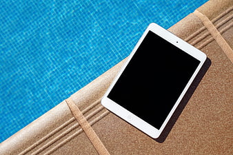 White tablet on poolside lounge chair with blue water background