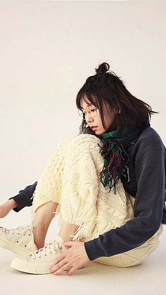 Young woman in cozy knitwear sitting on white background