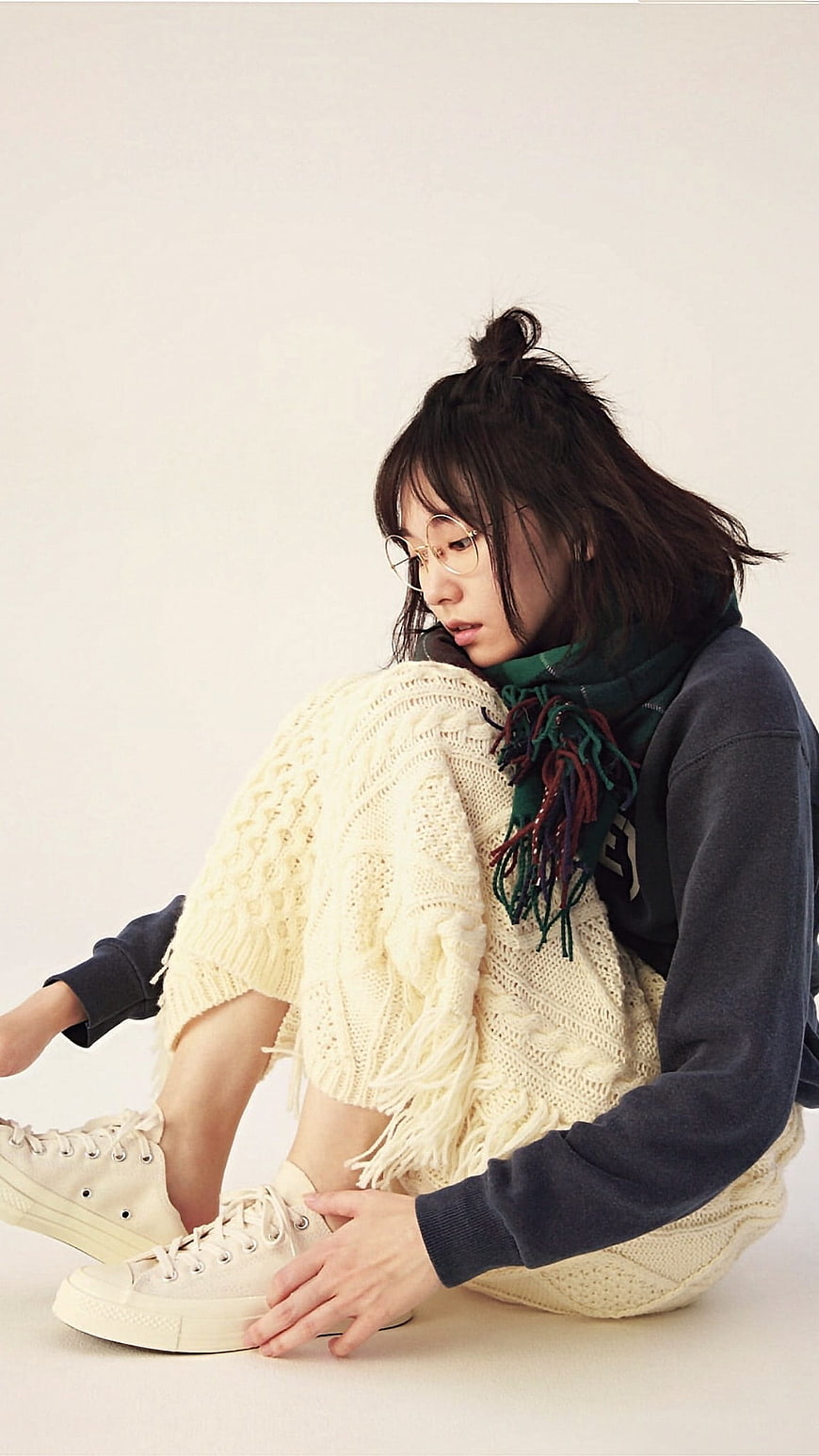 Young woman in cozy knitwear sitting on white background