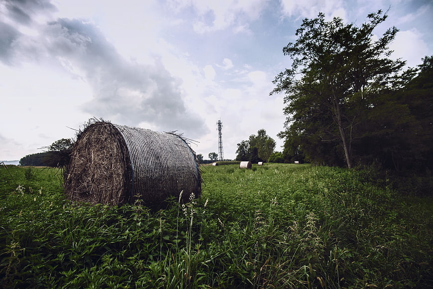 Round Hay Bale in Green Field Under Cloudy Sky
