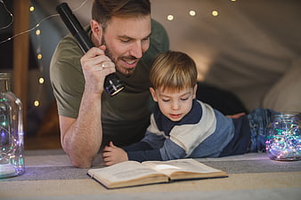 Father and son reading with flashlight in indoor tent