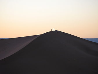Silhouettes of travelers on a sand dune at sunset