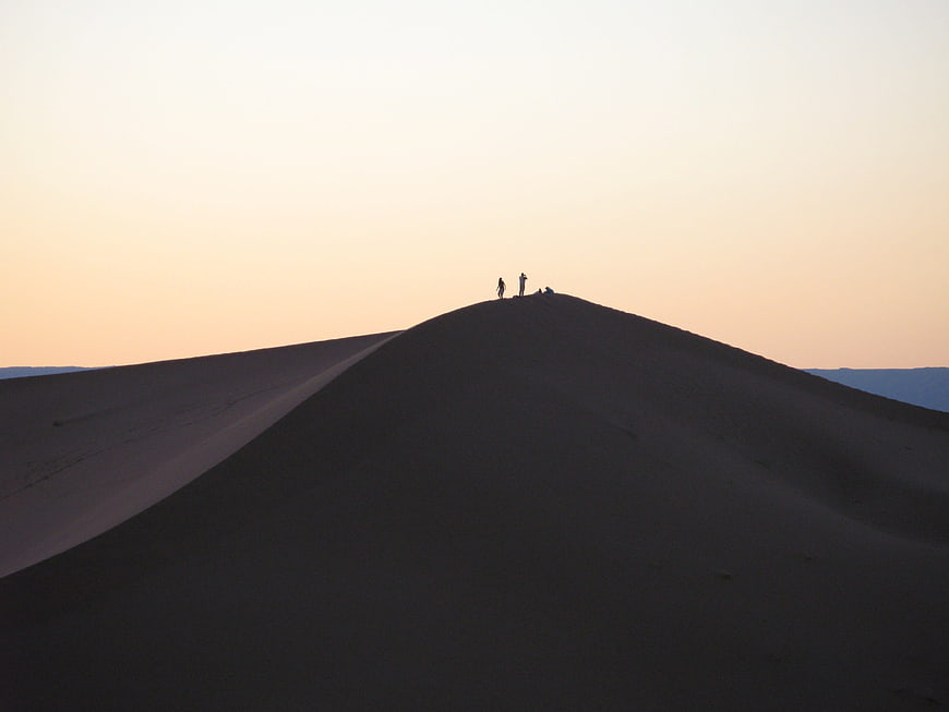 Silhouettes of travelers on a sand dune at sunset