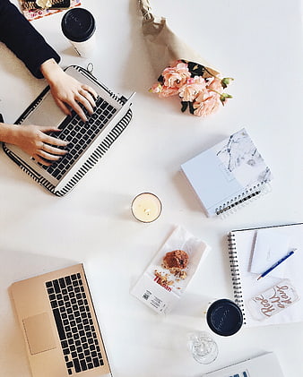 Flat lay of workspace with laptops, flowers, and coffee