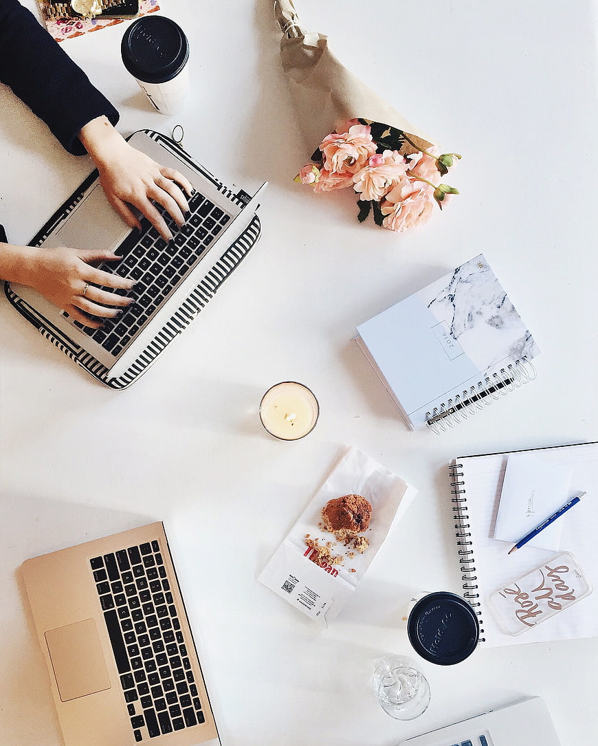 Flat lay of workspace with laptops, flowers, and coffee