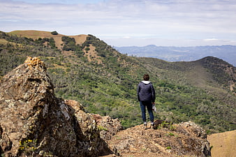 Hiker Standing on Rocky Cliff Overlooking Green Hills