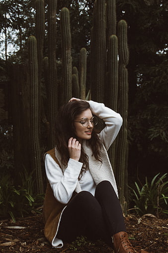 Woman with glasses sitting in front of tall cacti