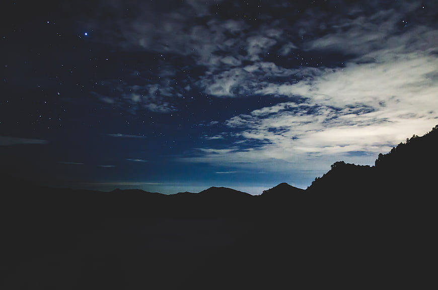 Silhouette of mountains under a starry night sky with clouds