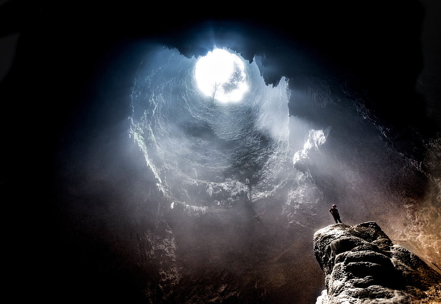 Silhouette of Man Standing in Massive Cave with Light Beams