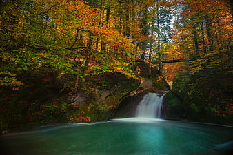 Autumn waterfall in forest with turquoise pool and colorful foliage