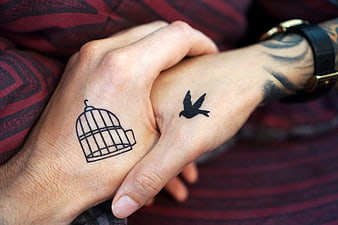 Couple holding hands with matching birdcage and bird tattoos