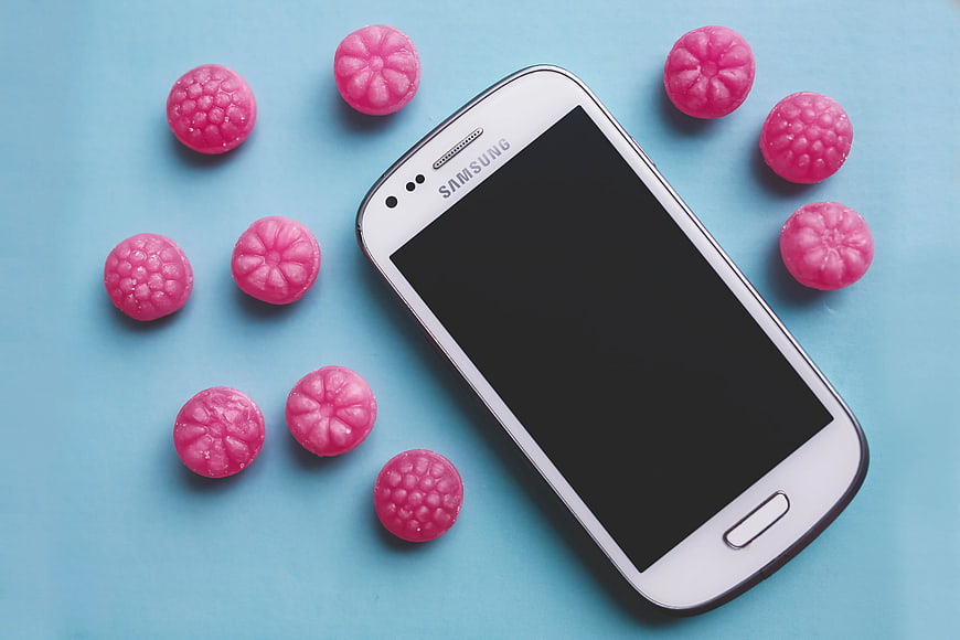White smartphone mockup with pink candies on blue background