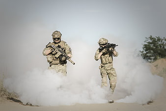Two soldiers in tactical gear advancing through smoke in desert