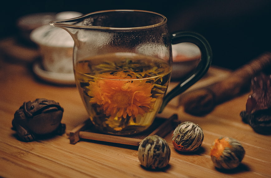 Glass teapot with blooming chrysanthemum tea on wooden table