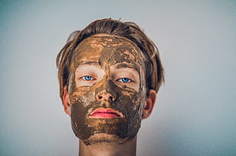 Man with brown clay face mask and blue eyes
