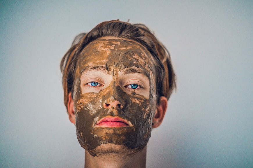 Man with brown clay face mask and blue eyes