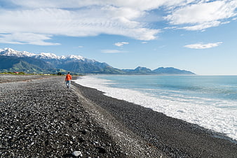 Man Walking on Pebble Beach with Snowy Mountains