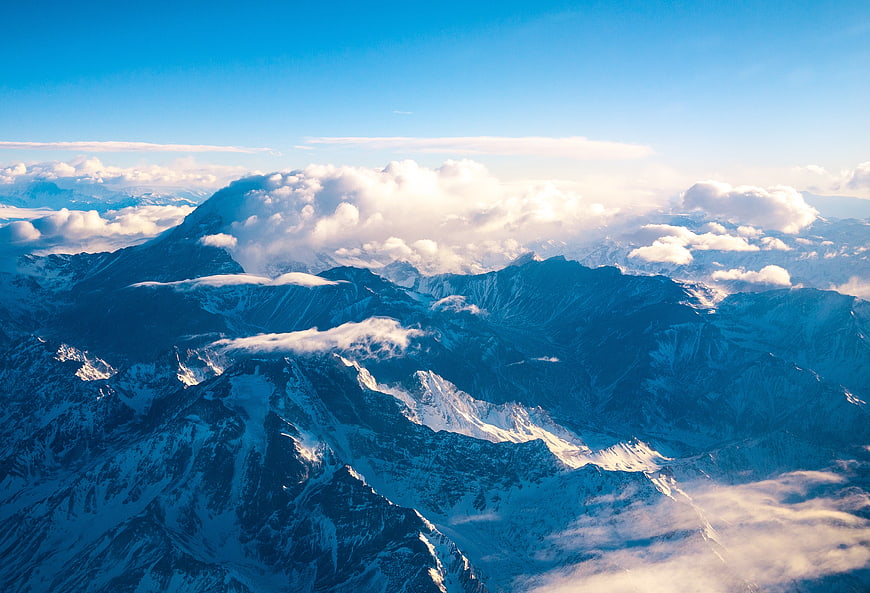 Aerial View of Snow-Capped Mountain Peaks Above Clouds