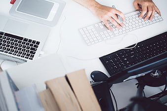 Overhead view of hands typing on multiple keyboards at a white desk