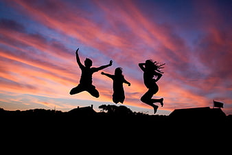 Silhouettes of three friends jumping against a vibrant sunset sky