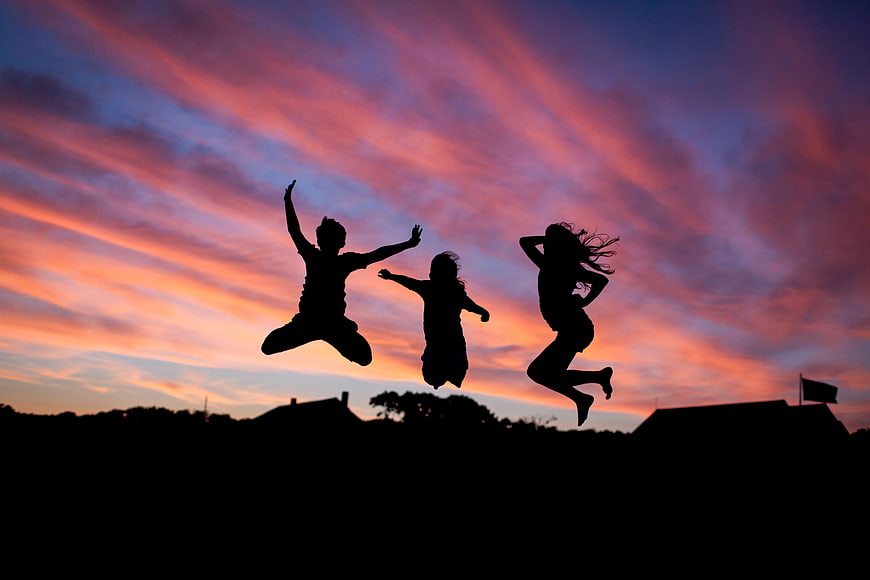 Silhouettes of three friends jumping against a vibrant sunset sky