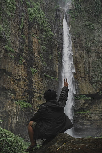 Backpacker posing with peace sign at misty waterfall