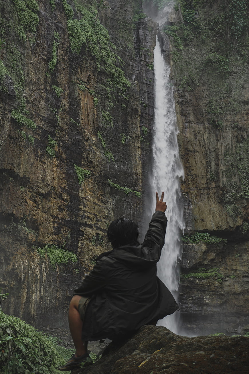 Backpacker posing with peace sign at misty waterfall