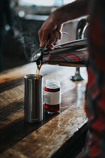 Pouring Hot Coffee into Travel Mug on Wooden Counter