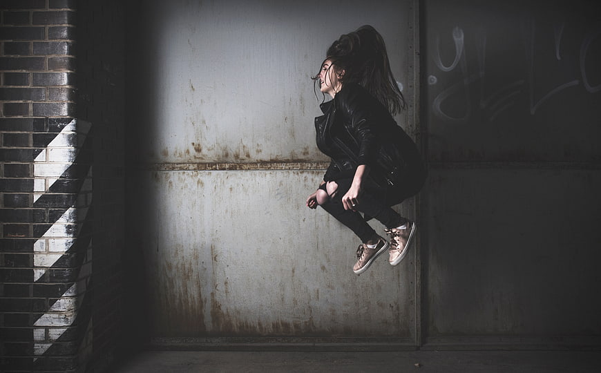 Woman jumping in dark urban alley with graffiti