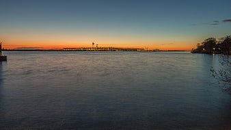 Sunset over industrial waterfront with calm water and city lights