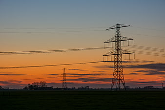 Silhouette of electricity pylons against vibrant orange sunset sky