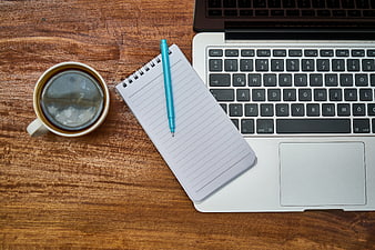 Flat lay of laptop, notebook, pen, and coffee on wooden desk